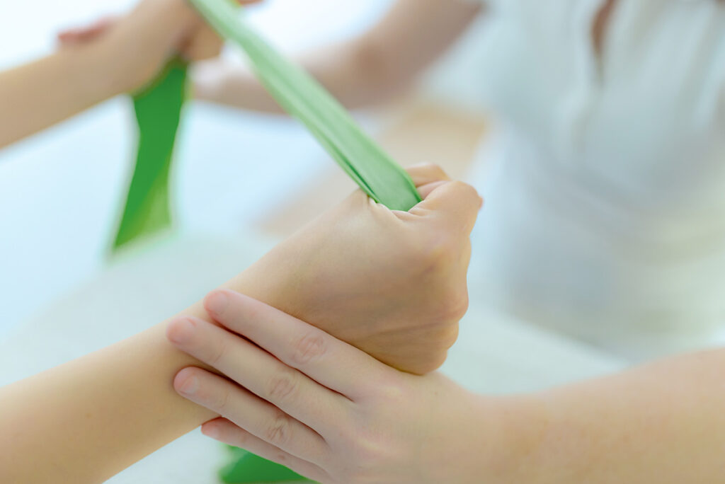 Krankengymnastik - Physiotherapeutin macht Übungen mit Theraband